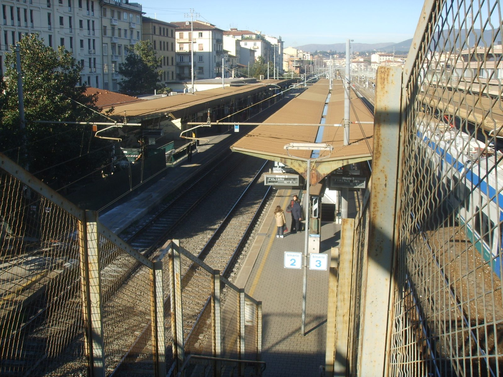 I binari e le pensiline della stazione di Firenze Campo di Marte visti dal sovrappasso pedonale, con i palazzi del quartiere e le colline sullo sfondo