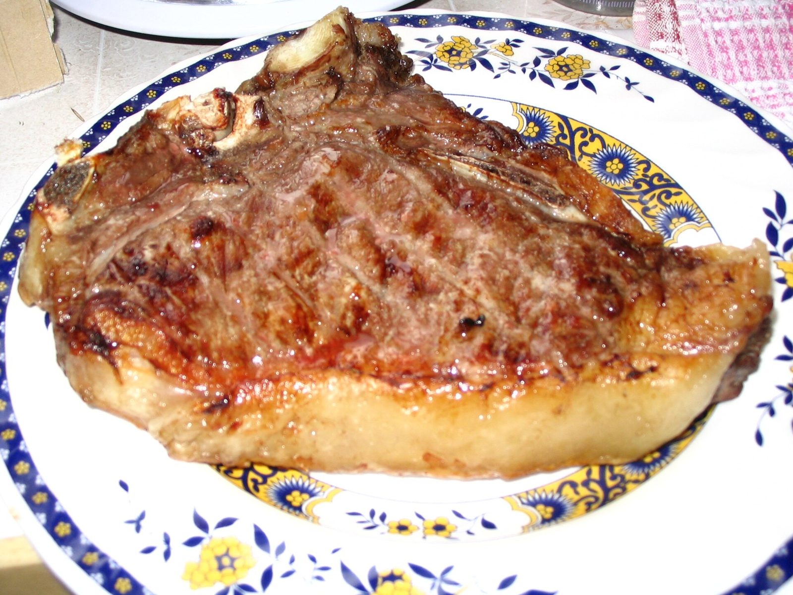 Bistecca alla fiorentina con l'osso a T, grigliata e dorata, servita su un piatto bianco con decori blu e gialli